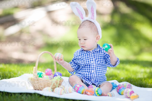 mixed-race chinese and caucasian baby boy outside wearing rabbit ears playing with easter eggs