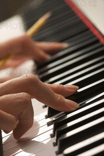 Woman's fingers with pencil on digital piano keys