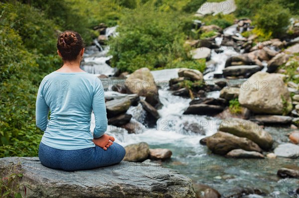 Woman in Hatha yoga asana Padmasana outdoors at tropical waterfall