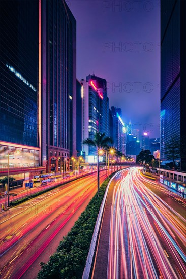 Street traffic in Hong Kong at night. Office skyscraper buildings and busy traffic on highway road with blurred cars light trails. Hong Kong