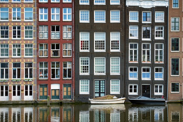 Row of typical houses and boat on Amsterdam canal Damrak with reflection. Amsterdam