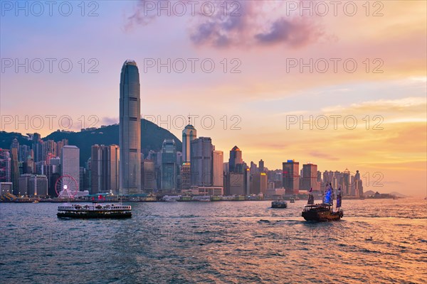 Hong Kong skyline cityscape downtown skyscrapers over Victoria Harbour in the evening with ferry boat and junk boat on sunset. Hong Kong