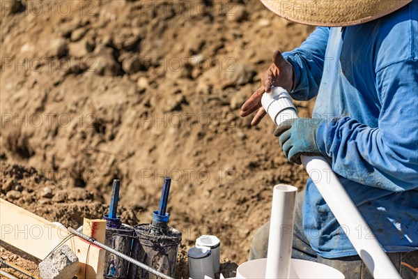 Plumber applying glue to PVC pipe at construction site