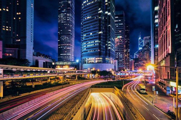 Street traffic in Hong Kong at night. Office skyscraper buildings and busy traffic on highway road with blurred cars light trails. Hong Kong