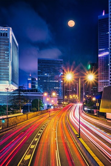 Street traffic in Hong Kong at night. Office skyscraper buildings and busy traffic on highway road with blurred cars light trails. Hong Kong