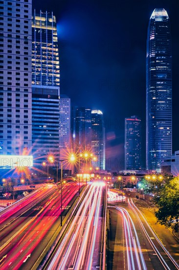 Street traffic in Hong Kong at night. Office skyscraper buildings and busy traffic on highway road with blurred cars light trails. Hong Kong