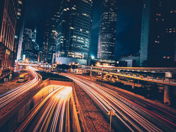 Street traffic in Hong Kong at night. Office skyscraper buildings and busy traffic on highway road with blurred cars light trails. Hong Kong