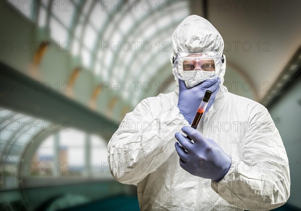 Man wearing HAZMAT protective clothing holding test tube filled with blood inside building