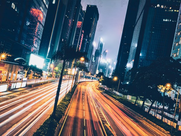 Street traffic in Hong Kong at night. Office skyscraper buildings and busy traffic on highway road with blurred cars light trails. Hong Kong