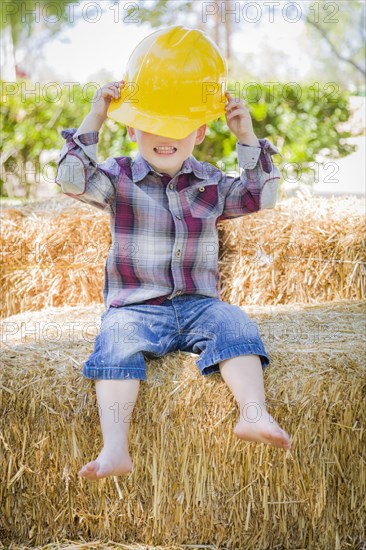 Cute young mixed-race boy laughing with hard hat outside sitting on hay bale