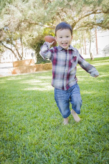 Cute young mixed-race boy playing football outside at the park