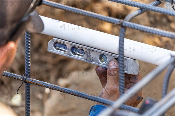 Plumber using level while installing PVC pipe at construction site