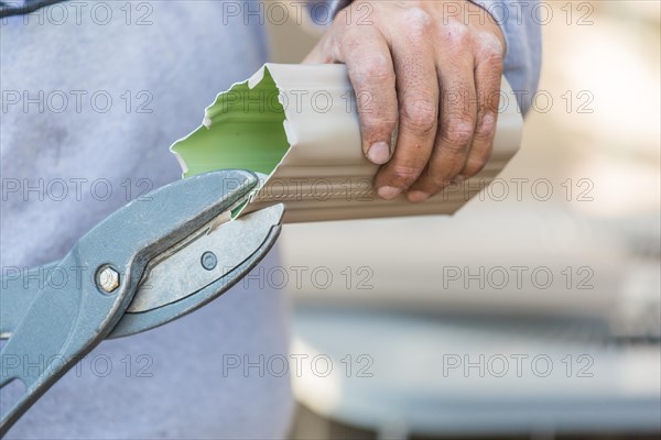 Worker cutting aluminum rain gutter with heavy shears