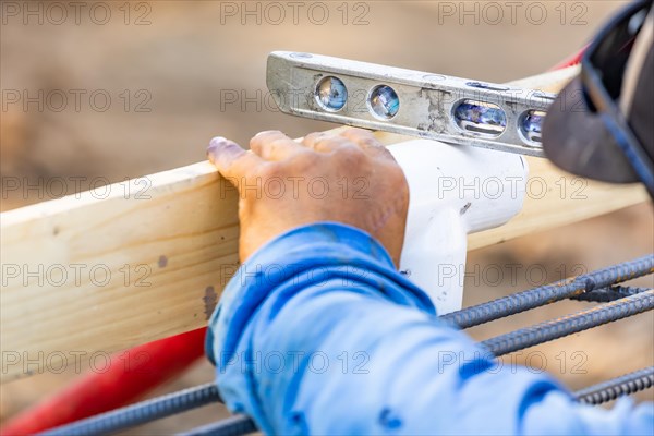Plumber using level while installing PVC pipe at construction site