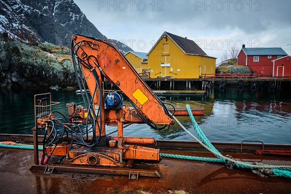 Crane on pier in Nusfjord authentic fishing village in winter with red rorbu houses. Lofoten islands