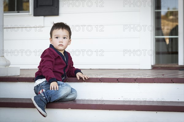 Cute melancholy mixed-race boy sitting on front porch steps