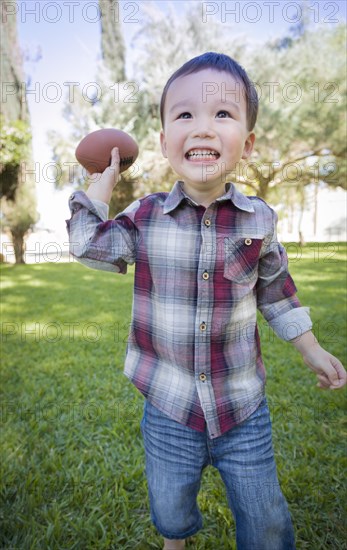Cute young mixed-race boy playing football outside at the park