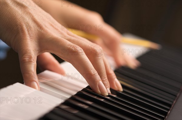 Woman's fingers with pencil on digital piano keys