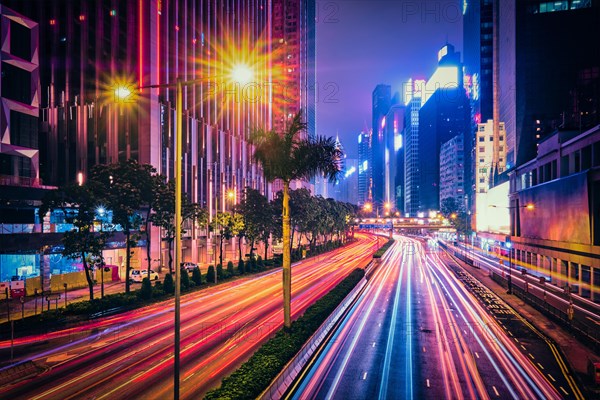 Street traffic in Hong Kong at night. Office skyscraper buildings and busy traffic on highway road with blurred cars light trails. Hong Kong