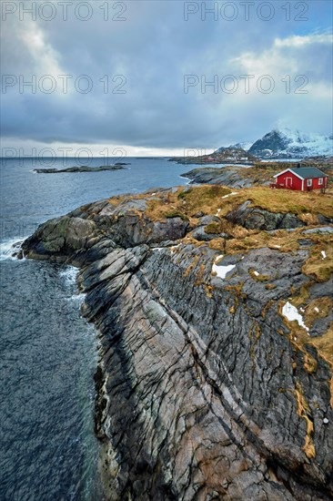 Clif with traditional red rorbu house on Litl-Toppoya islet on Lofoten Islands