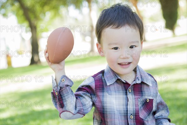 Cute young mixed-race boy playing football outside at the park