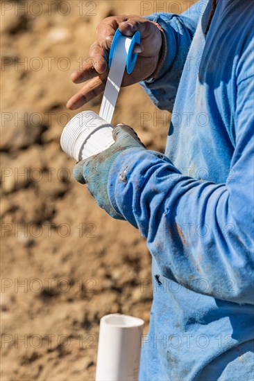 Plumber applying PTFE tape to PVC pipe at construction site