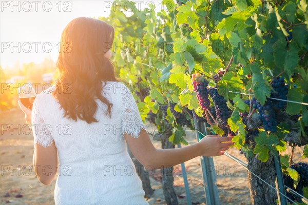 Young adult woman enjoying glass of wine tasting walking in the vineyard