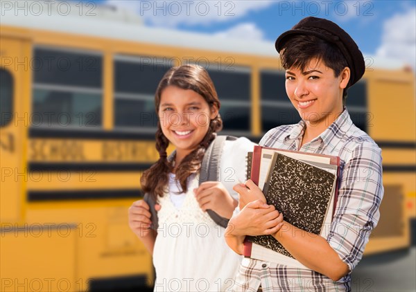 Young mixed-race female students near school bus