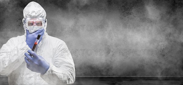 Man wearing hazmat suit and goggles holding test tube of blood in smokey room banner with copy space