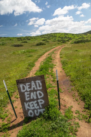 Dead end keep out sign on wire fence at dirt road