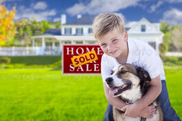 Happy young boy and his dog in front of sold for sale real estate sign and house