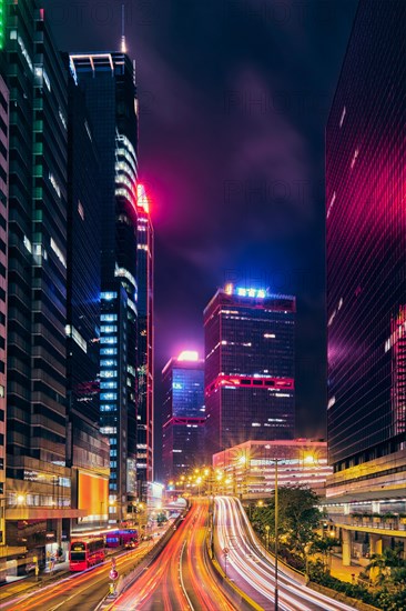 Street traffic in Hong Kong at night. Office skyscraper buildings and busy traffic on highway road with blurred cars light trails. Hong Kong