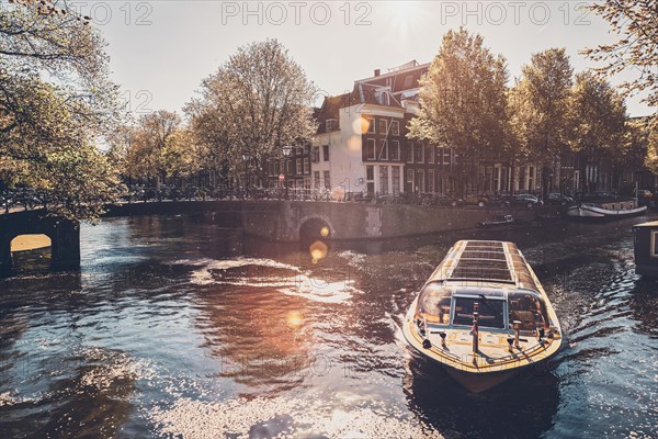 Amsterdam canal with tourist boat and old houses on sunset. Amsterda