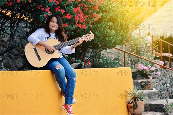 Pretty smiling girl sitting playing guitar outdoors