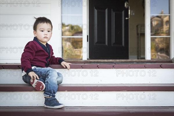 Cute melancholy mixed-race boy sitting on front porch steps