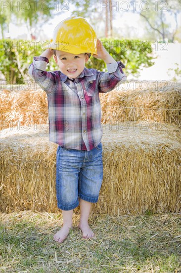 Cute young mixed-race boy laughing with hard hat outside near hay bale