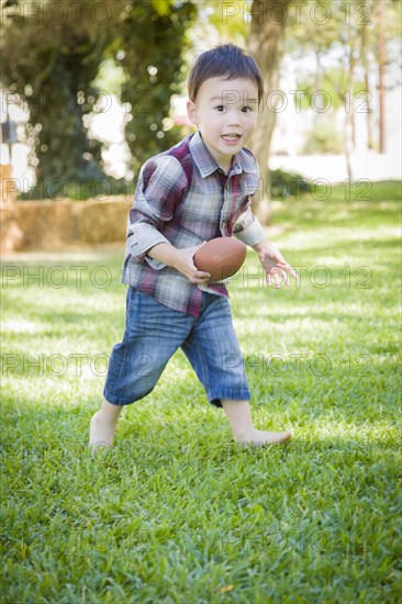 Cute young mixed-race boy playing football outside at the park