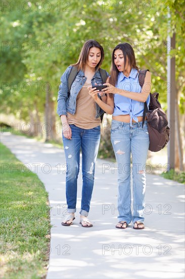 Two beautiful young ethnic twin sisters with backpacks using A smartphone outside