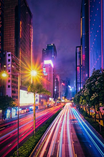 Street traffic in Hong Kong at night. Office skyscraper buildings and busy traffic on highway road with blurred cars light trails. Hong Kong