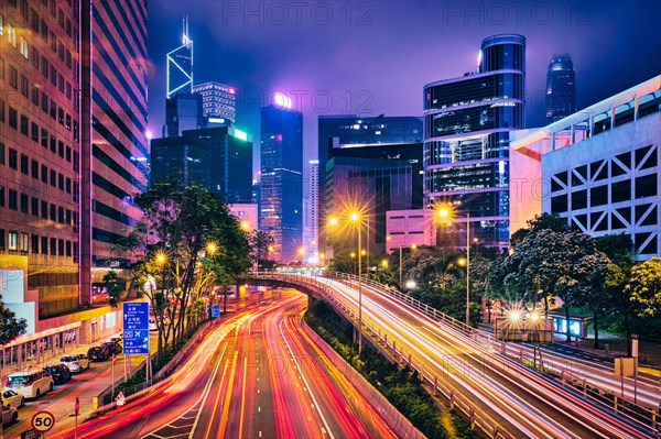 Street traffic in Hong Kong at night. Office skyscraper buildings and busy traffic on highway road with blurred cars light trails. Hong Kong