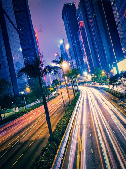 Street traffic in Hong Kong at night. Office skyscraper buildings and busy traffic on highway road with blurred cars light trails. Hong Kong