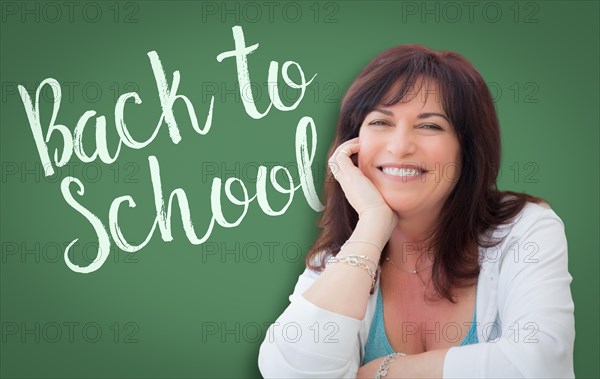 Back to school written on green chalkboard behind smiling middle aged woman