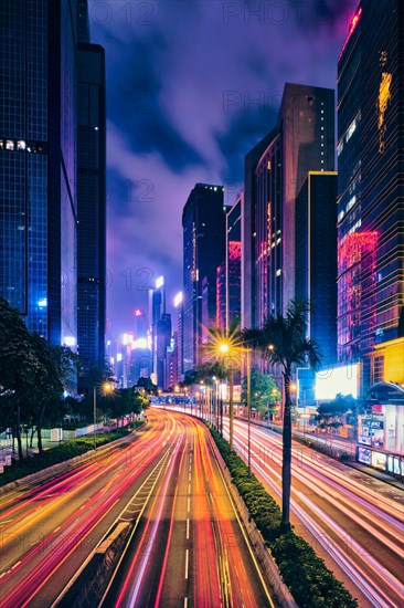 Street traffic in Hong Kong at night. Office skyscraper buildings and busy traffic on highway road with blurred cars light trails. Hong Kong