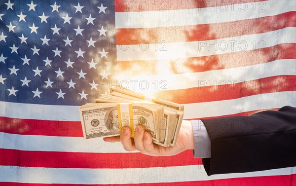 Hand holding stacks of cash in front of american flag