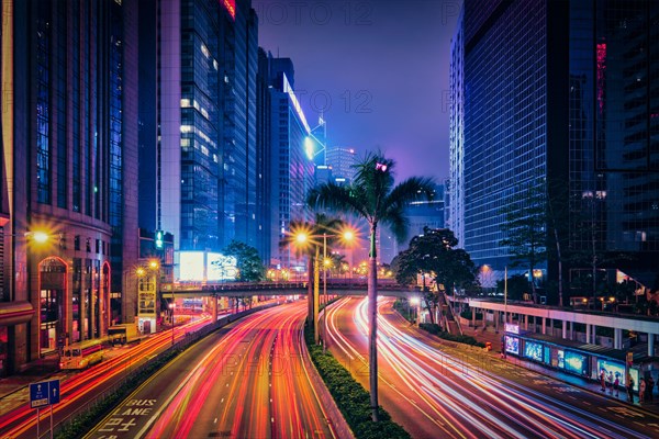 Street traffic in Hong Kong at night. Office skyscraper buildings and busy traffic on highway road with blurred cars light trails. Hong Kong