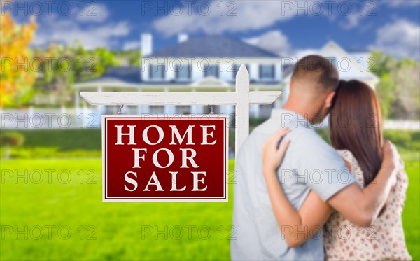 For sale real estate sign and affectionate military couple looking at nice new house