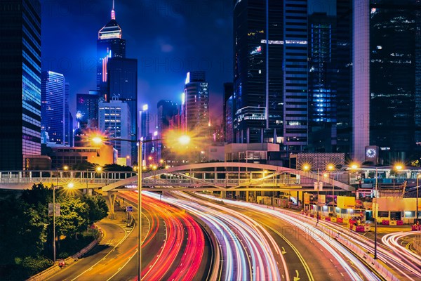 Street traffic in Hong Kong at night. Office skyscraper buildings and busy traffic on highway road with blurred cars light trails. Hong Kong