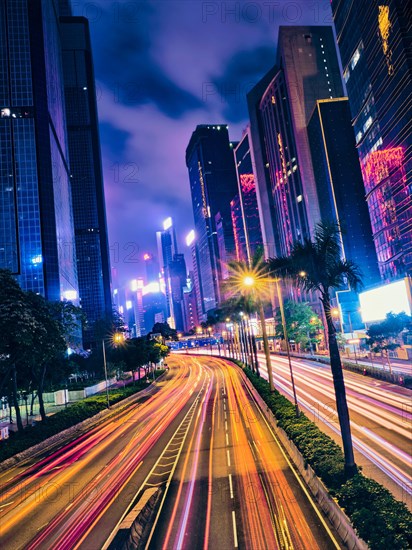 Street traffic in Hong Kong at night. Office skyscraper buildings and busy traffic on highway road with blurred cars light trails. Hong Kong