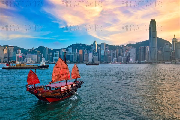 Hong Kong skyline cityscape downtown skyscrapers over Victoria Harbour in the evening with junk tourist ferry boat on sunset with dramatic sky. Hong Kong