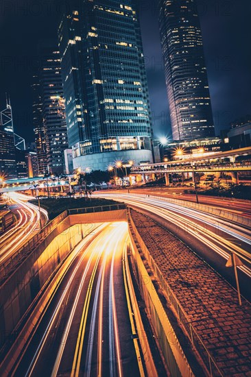 Street traffic in Hong Kong at night. Office skyscraper buildings and busy traffic on highway road with blurred cars light trails. Hong Kong